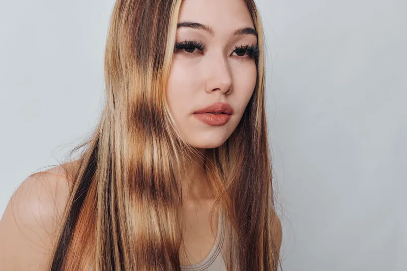 Young woman with long straight hair and natural makeup wearing a sleeveless top posing against light background. Beauty, portrait and fashion concept with casual style.