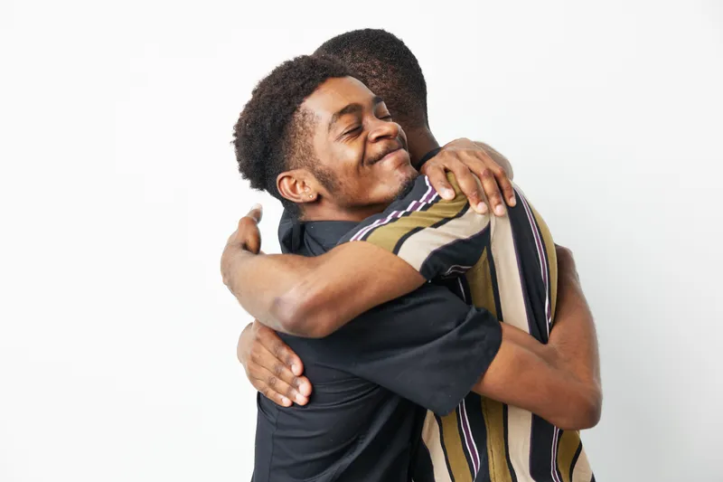 Black men embracing each other in a moment of joy and connection, celebrating friendship and love with warm smiles and genuine expressions.