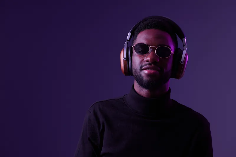 Confident young man wearing sunglasses and headphones, posing against a purple background, showcasing modern style and urban fashion, perfect for music and lifestyle themes