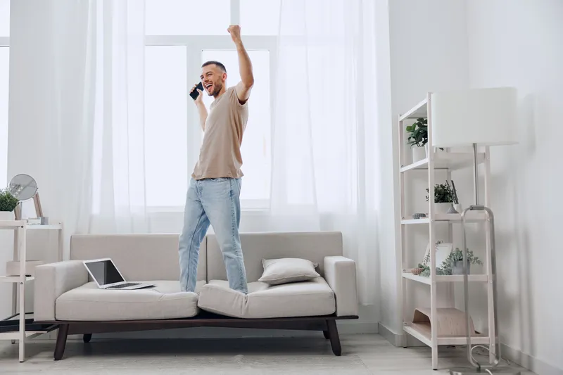 Excited man celebrating a positive phone call, reflecting on mental health and the importance of emotional connections in a cozy home environment.