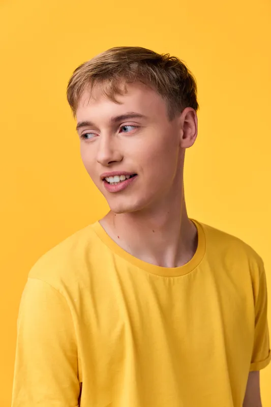 Casual young man with a warm smile wearing a yellow tee against a vibrant yellow studio background natural pose soft lighting ideal for lifestyle and fashion projects