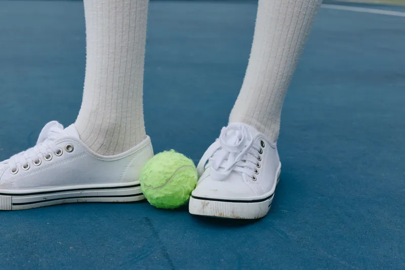 Young athlete s feet in white sneakers on tennis court with vibrant green tennis ball, showcasing sporty lifestyle and energetic vibes