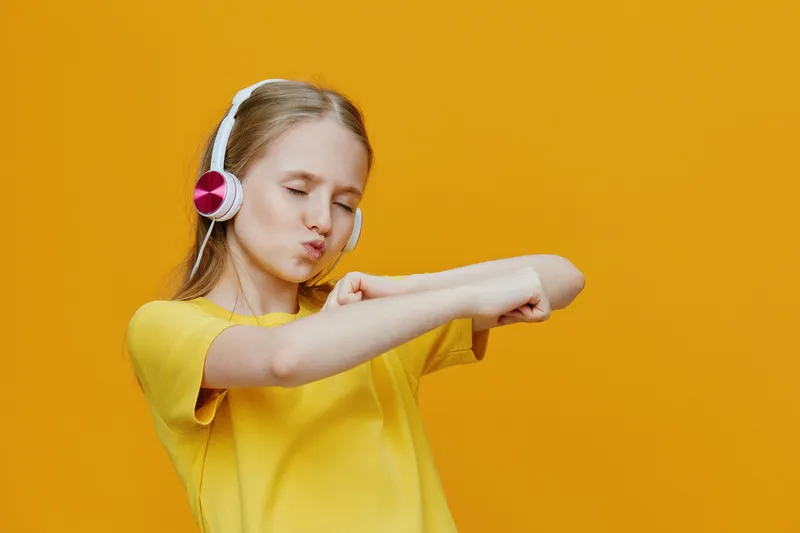 Happy girl in yellow t shirt dancing with headphones on a vibrant yellow background, expressing joy and music enjoyment
