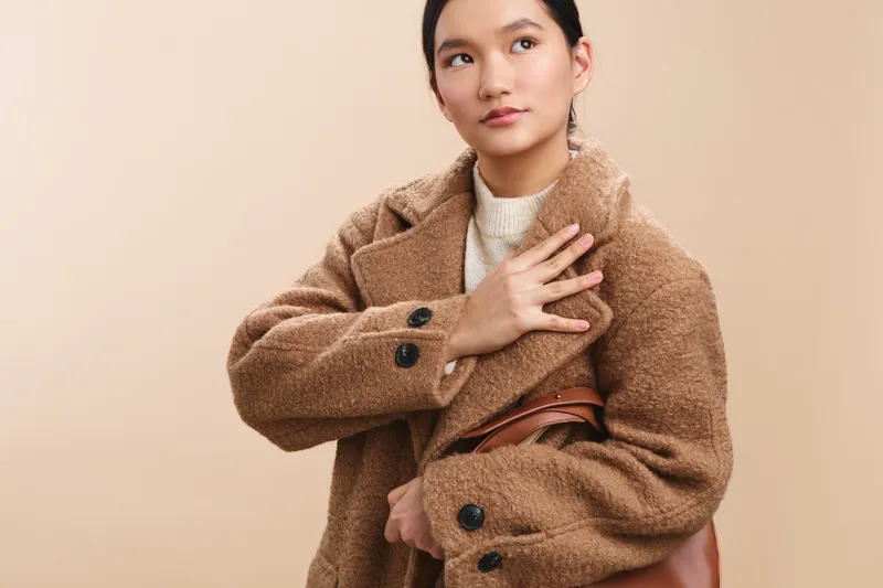 asian woman models a chic textured coat in a neutral studio setting, exuding understated elegance and poised confidence.