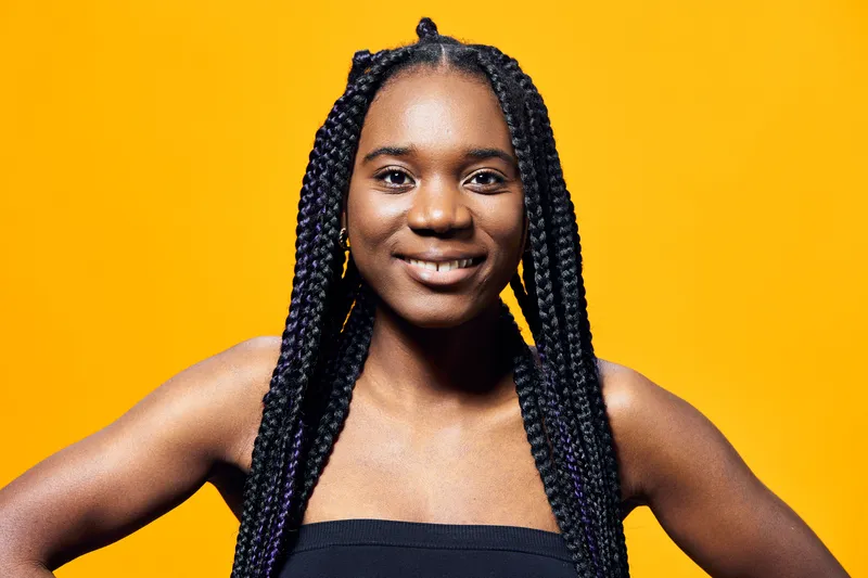 Portrait of a smiling Black woman with braided hair against a vibrant yellow background, showcasing joy and confidence in a modern style