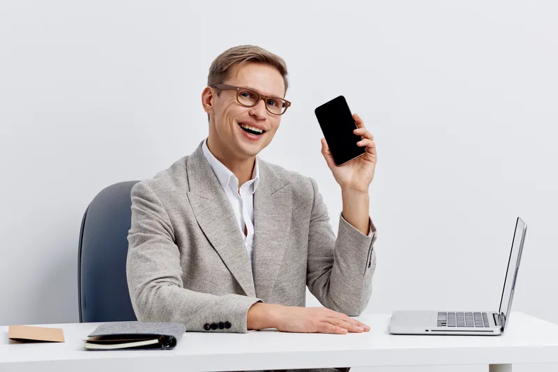 smiling caucasian man working with phone laptop at desk talk on video call remote work cybersecurity concept