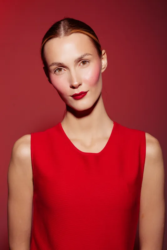 Portrait of a confident woman with slicked hair wearing a red sleeveless top against a red background. Concept of fashion, beauty, elegance, and minimalism in studio lighting.