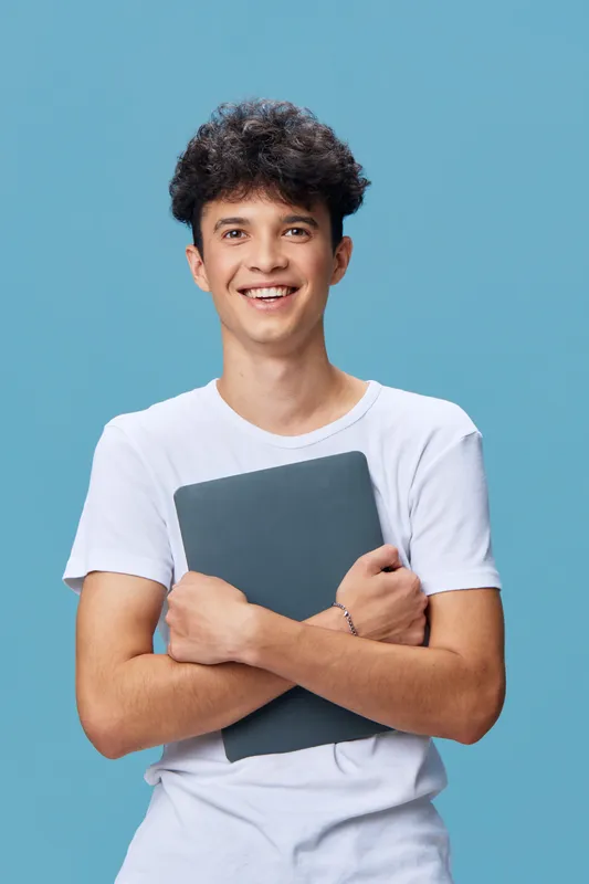 Smiling man wearing white t-shirt holding laptop against blue background, expressing confidence and friendliness in casual style digital technology concept.
