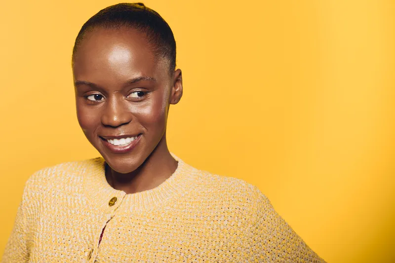 Smiling dark skinned African woman in yellow knitted sweater poses against bright yellow background. Concept of happiness, fashion, beauty, and confident female portrait in studio lighting.