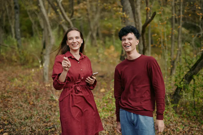 Two friends walk through a sunlit autumn forest, sharing a candid moment of laughter and connection, conveying authenticity, credibility, and a warm, relatable mood in everyday life.