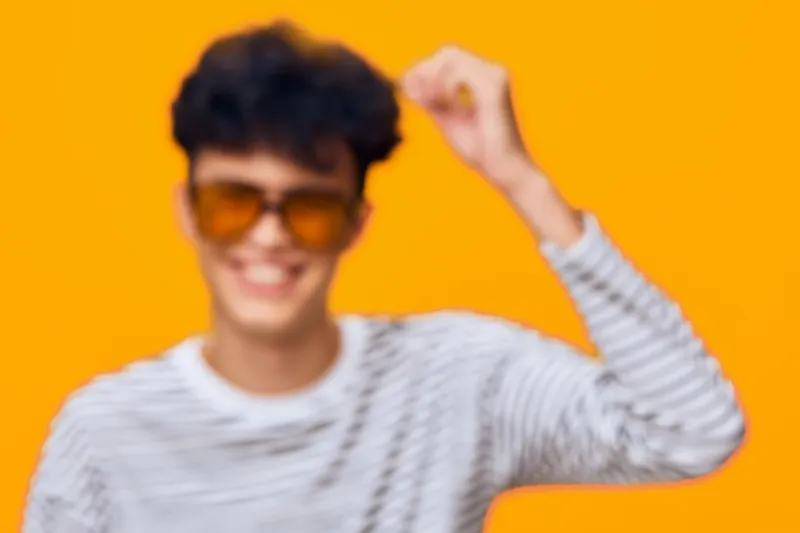 Smiling man wearing sunglasses and striped shirt poses happily against bright orange background, radiating positive energy and casual style in vibrant studio setting.