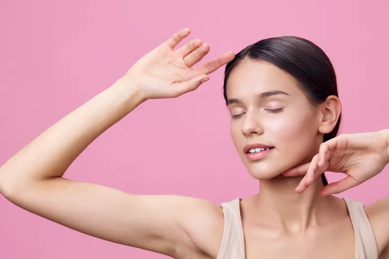 Young woman with closed eyes, soft smile, and elegant pose against a pink background, showcasing beauty and confidence in fashion and lifestyle photography