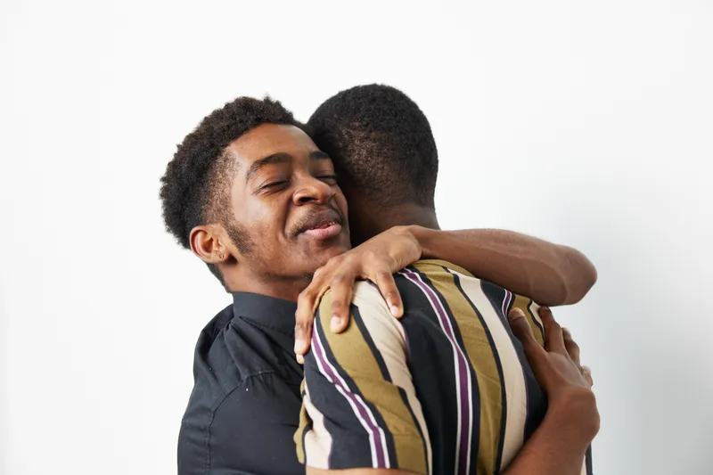 Two African American men embracing each other in a heartfelt moment, showcasing love and friendship against a clean white background.
