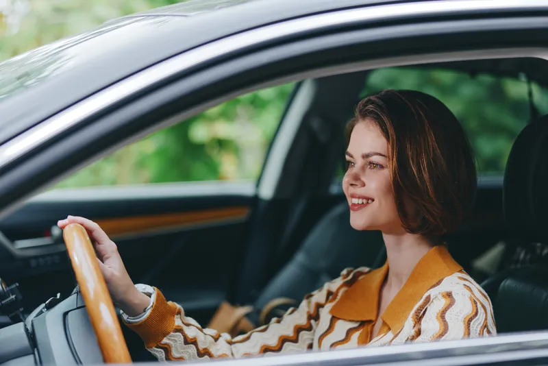 Portrait of a smiling woman behind the wheel, hands on the steering wheel, inside a car, conveying confidence and calm during a drive.