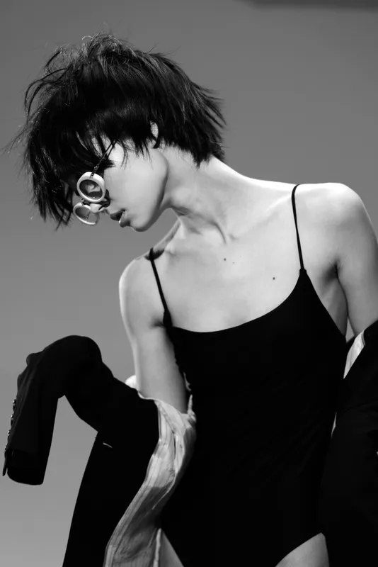 Black and white portrait of a young woman with short hair wearing glasses and a camisole, showcasing modern fashion and minimalistic style.