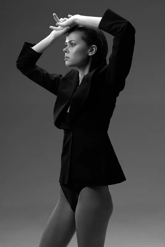 Black and white portrait of a woman posing confidently in stylish blazer and bodysuit, showcasing elegance and strength.