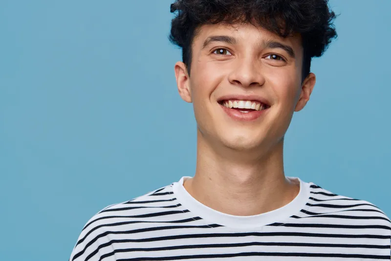 smiling man with curly hair wearing a striped shirt, bright blue background, cheerful mood, casual style, youthful expression, studio portrait lighting