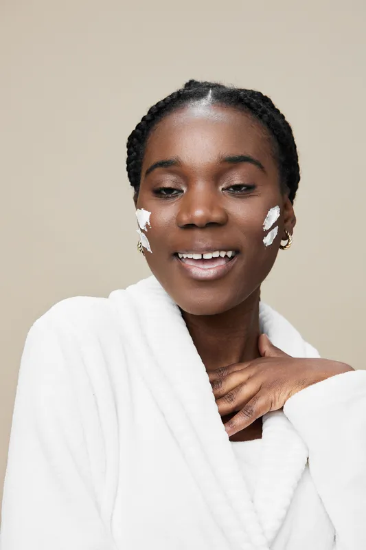 Smiling young woman applying skincare cream on her face, showcasing a glowing complexion and a serene atmosphere, perfect for beauty and self care concepts