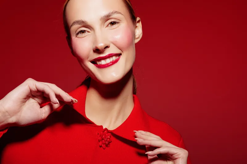 Smiling woman in red sweater poses against red background, showing joyful expression and natural makeup. Concept of happiness, fashion, and vibrant lifestyle with bright colors.