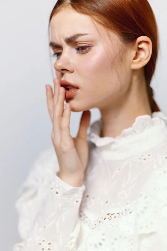 A thoughtful young woman with red hair in a white blouse expressing concern, showcasing emotions related to personal reflection and self awareness