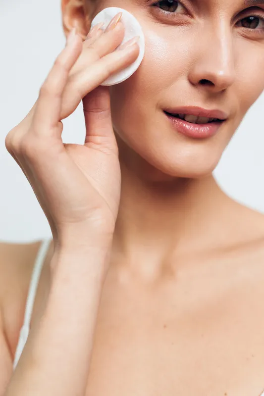 Close up of a woman applying a cotton pad to her cheek, showcasing skincare routine, clear skin, gentle cleansing, and a calm, fresh mood.
