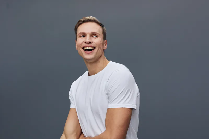 Smiling happy young man wearing white t-shirt look camera isolated on plain gray background studio portrait. People lifestyle concept, joyful emotion, casual style, male model, cheerful face, positive
