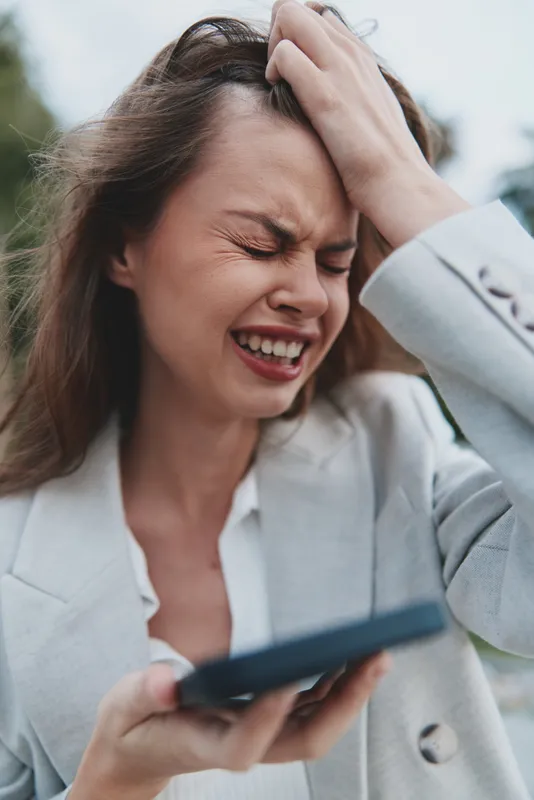 Professional woman experiencing stress while working on a smartphone in a business setting, showcasing emotions and style.