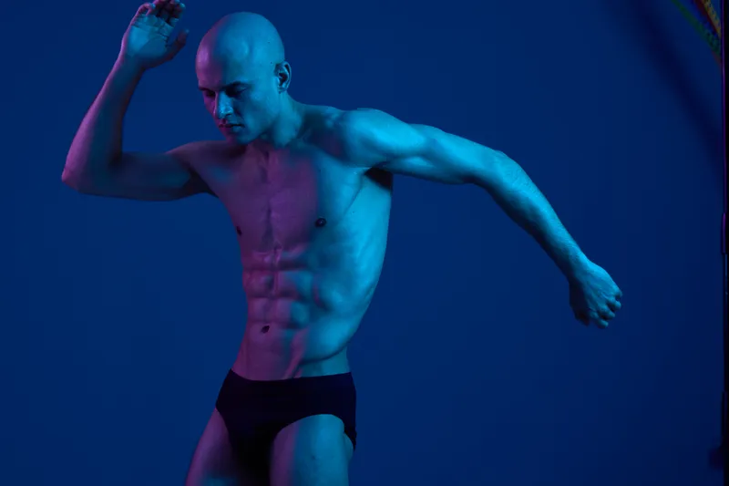 Strong man in black and white, showcasing athletic physique, with dynamic pose and dramatic lighting against a vibrant backdrop, emphasizing strength and movement.