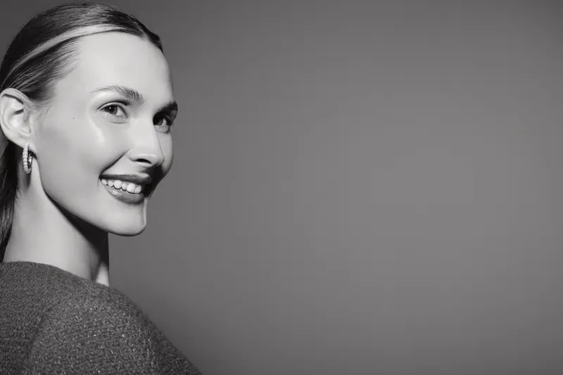 Smiling white woman with fair skin and light hair looks over shoulder with natural makeup in monochrome studio portrait. Concept of beauty, happiness, and elegance in minimal style.