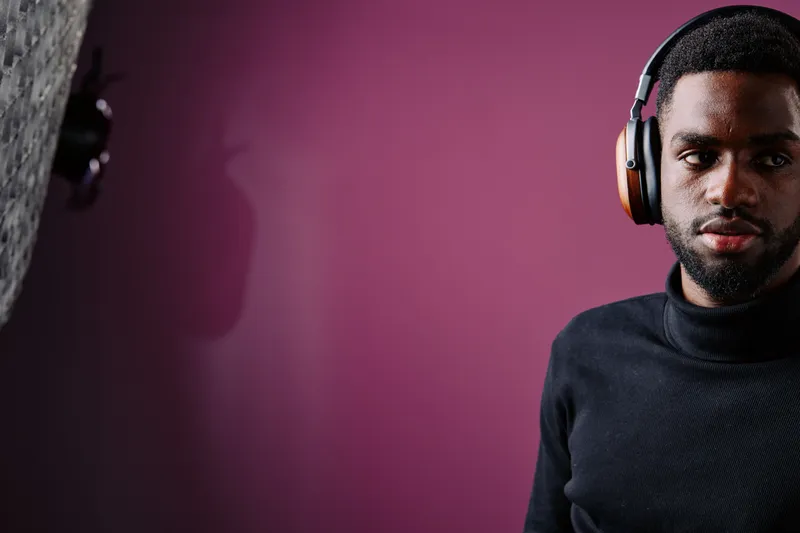 Young Black man wearing headphones, looking thoughtfully in a modern studio with a purple background, conveying deep concentration and style