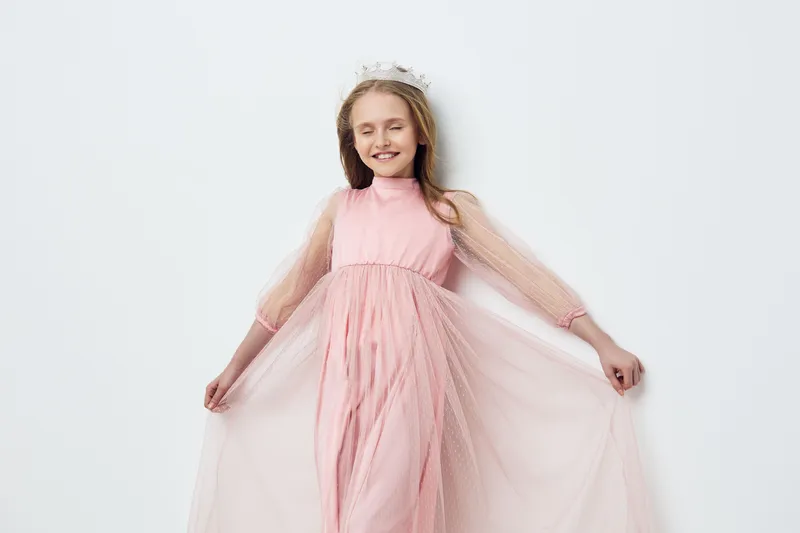 Young girl in a pink dress with tulle, smiling joyfully, against a light background, embodying innocence and happiness in springtime fashion