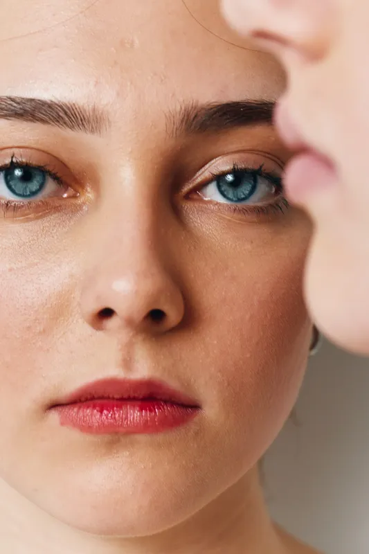 Closeup of woman with blue eyes and natural makeup looking at another blurred face in soft light for emotion and connection portrait.