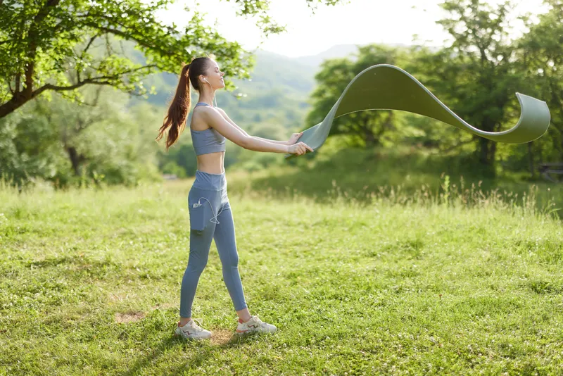 Young woman practicing outdoor fitness with resistance band in a green, grassy field, showcasing determination and healthy lifestyle in spring