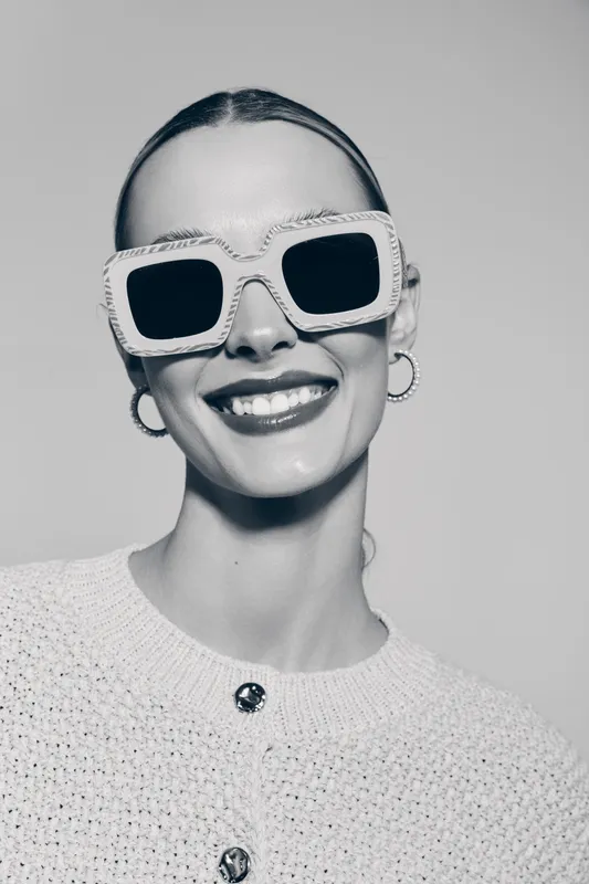 Smiling Caucasian woman with fair skin wearing oversized sunglasses and knitted sweater. Studio portrait with positive and fashionable mood.