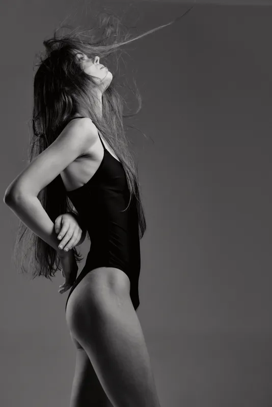 Black and white portrait of a young woman in a swimsuit with flowing hair, expressing freedom and elegance.