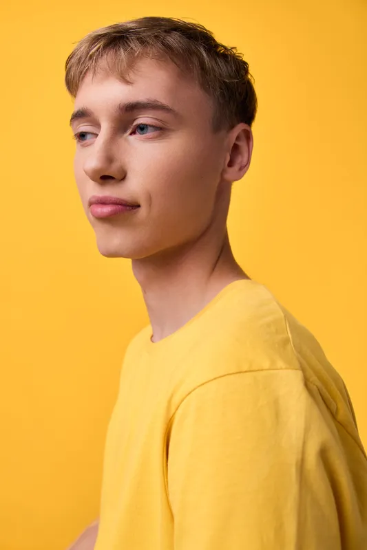 Young man in a yellow shirt against a yellow backdrop, studio fashion and lifestyle imagery with calm expression, clean lines, color harmony and contemporary styling