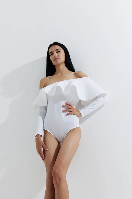 sport fitness woman in white stylish bodysuit posing confidently against plain background with natural light and minimalistic shadow, showcasing healthy lifestyle.