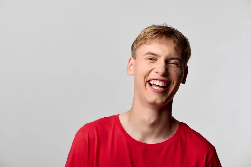 Smiling man in a red shirt against a neutral background, conveying happiness, confidence and casual vibe for lifestyle photography, studio lighting, and upbeat branding.