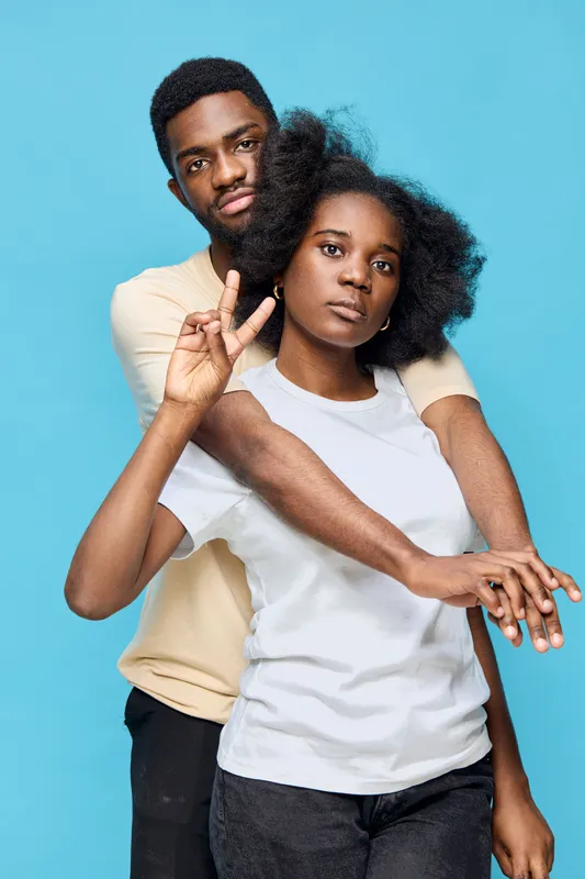 A young Black couple poses playfully against a vibrant blue background, showcasing joy, connection, and contemporary casual attire with a modern vibe