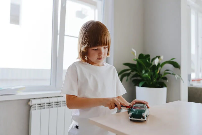 Curious boy playing with a toy car indoors, showcasing creativity and imagination in a bright, modern environment with plants and natural light.