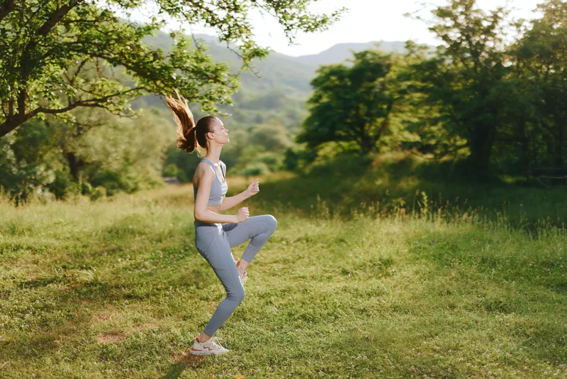 Young athletic woman jogging in the countryside, wearing blue sporty attire and showing determination against a lush green backdrop