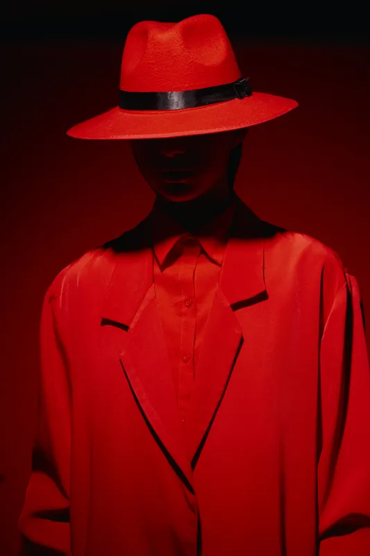 Stylish silhouette of a person wearing a bold red hat and matching coat in dramatic lighting with high contrast and shadows. Concept of fashion and beauty creative expression.