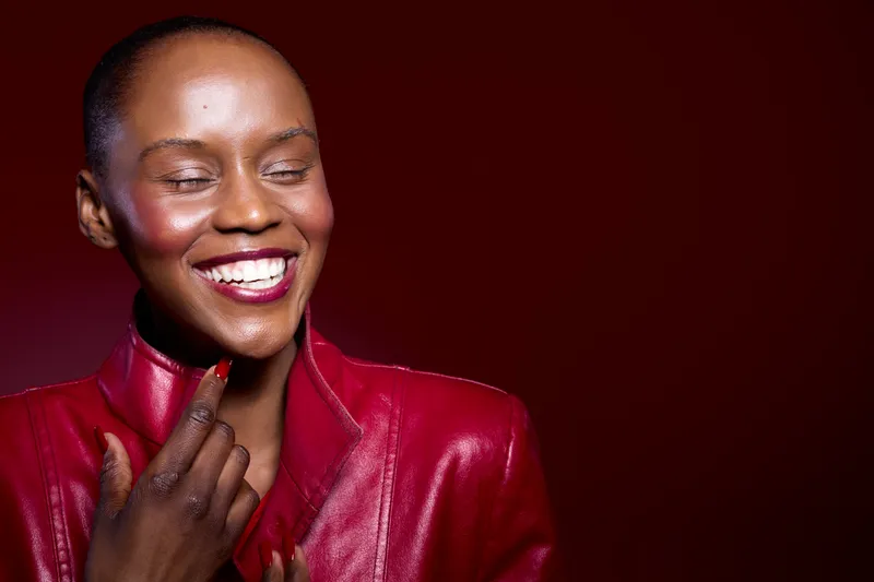 Smiling dark skinned African woman in red leather jacket looks down joyfully on purple background. Concept of happiness, fashion, beauty, and confident female portrait.