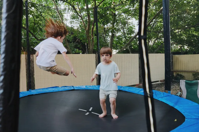 Active boys jumping on a trampoline in a backyard, showcasing joy and energy during playtime in a sunny environment.