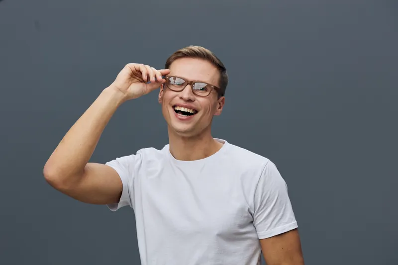 Smiling man wearing glasses white t-shirt laughing joy mental health gadgets happy casual lifestyle studio portrait