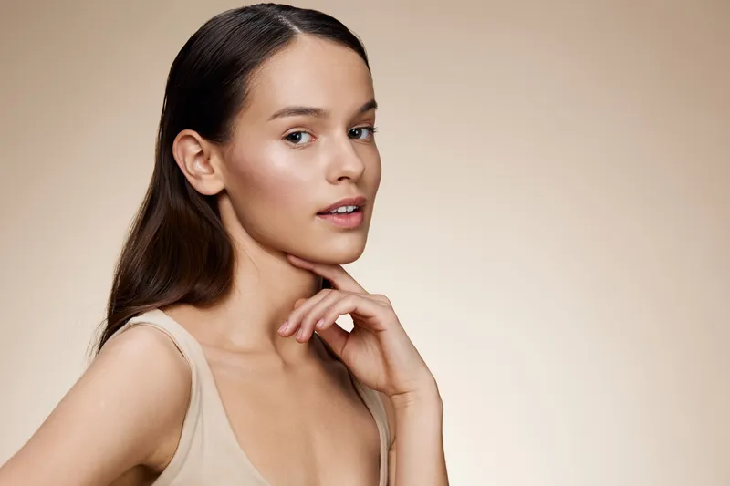 Close up portrait of a young woman with healthy skin and natural beauty on a soft beige background highlighting a minimalist aesthetic and glowing complexion