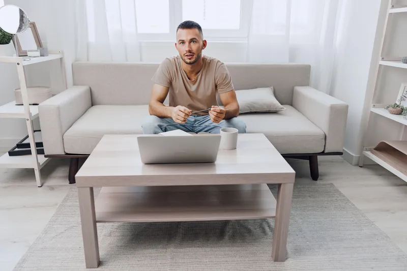 Thoughtful man relaxing in a modern living room while using a laptop, enjoying a cozy atmosphere and peaceful vibes. Ideal for content related to work-life balance.