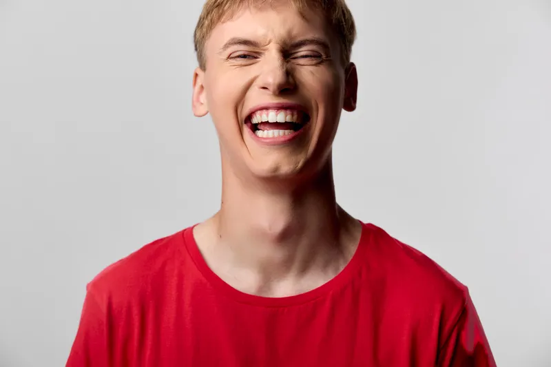 Laughter and a wide smile from a youth in a red shirt captures energetic mood, conveying happiness and authentic joy in a closeup, ideal for expressive lifestyle campaigns.