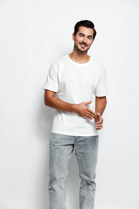 Full body smiling young caucasian man wearing white t-shirt look at camera with friendly expression, posing confidently on plain gray background. People lifestyle concept