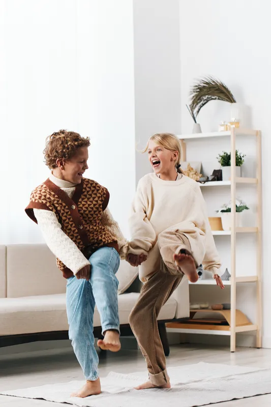 Two adults dance barefoot on a bright living room floor, sharing laughter and carefree energy while holding hands, embodying joy, connection, and spontaneous play.